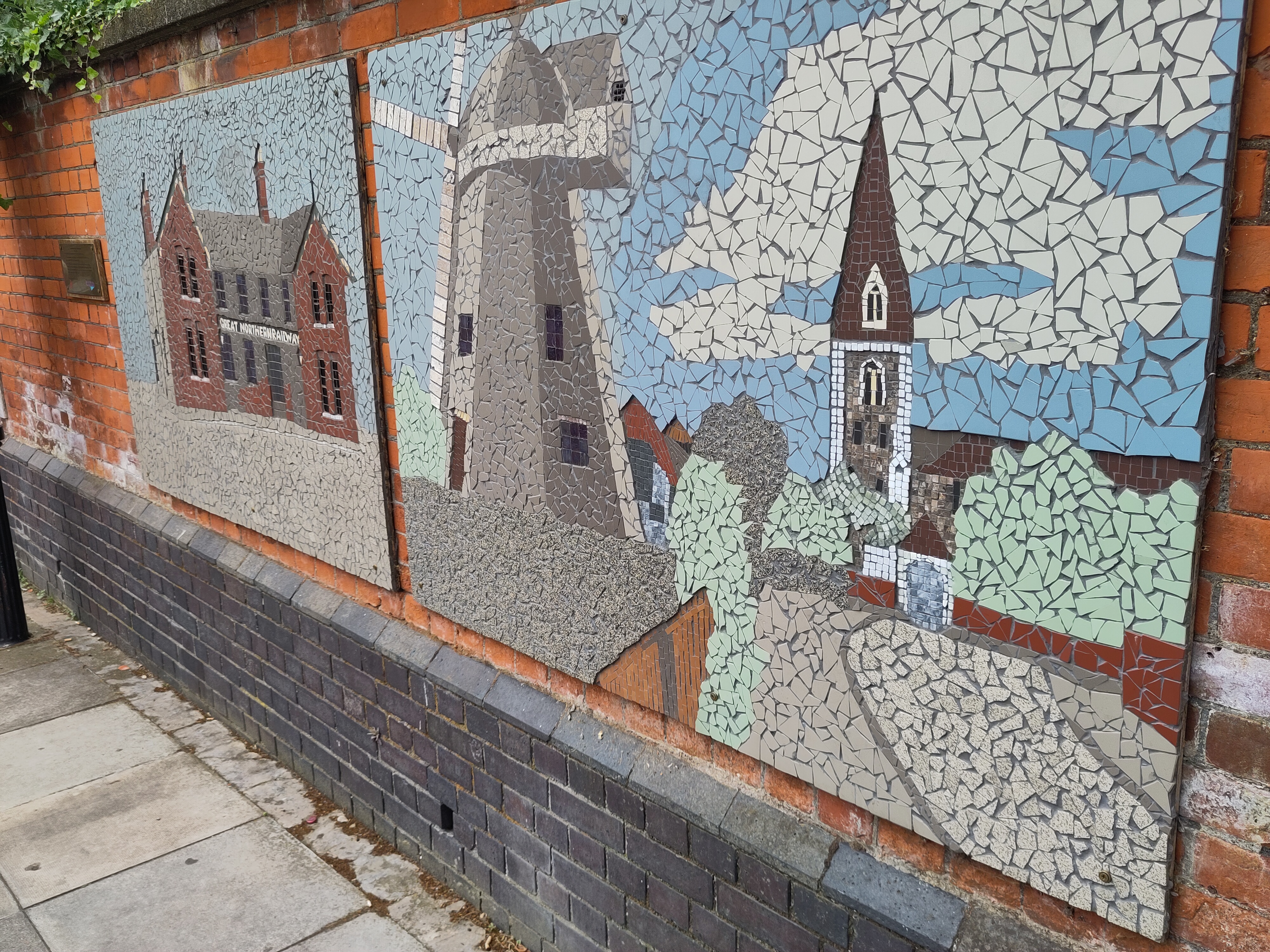 two mosaics on a brick wall, depicting a station and a smock mill