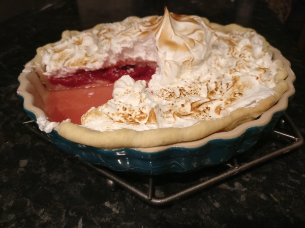 a meringue-topped pie with pink filling in a teal stoneware dish